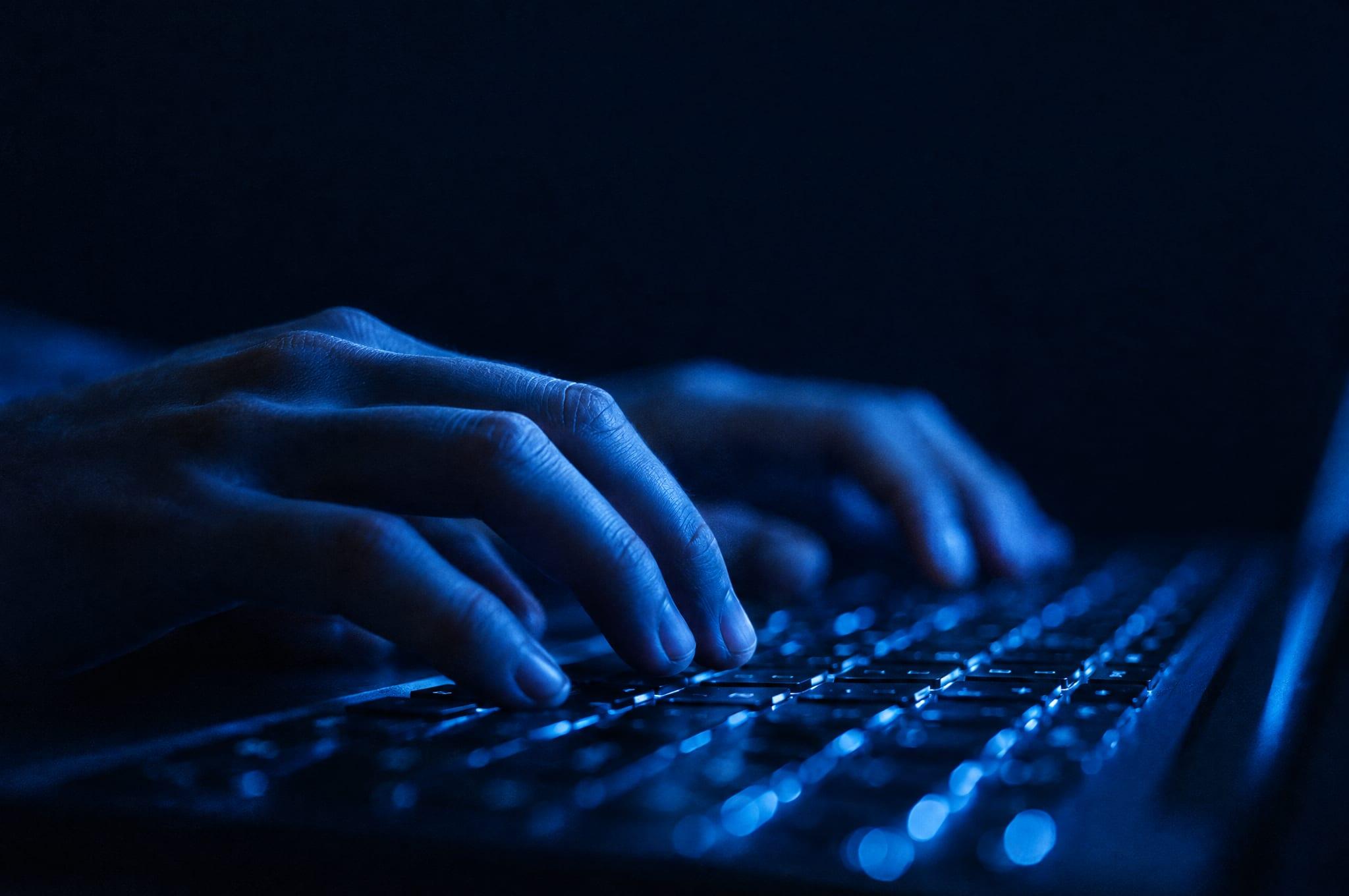 Close-up of hands typing on a laptop at night, lit by the screen’s glow